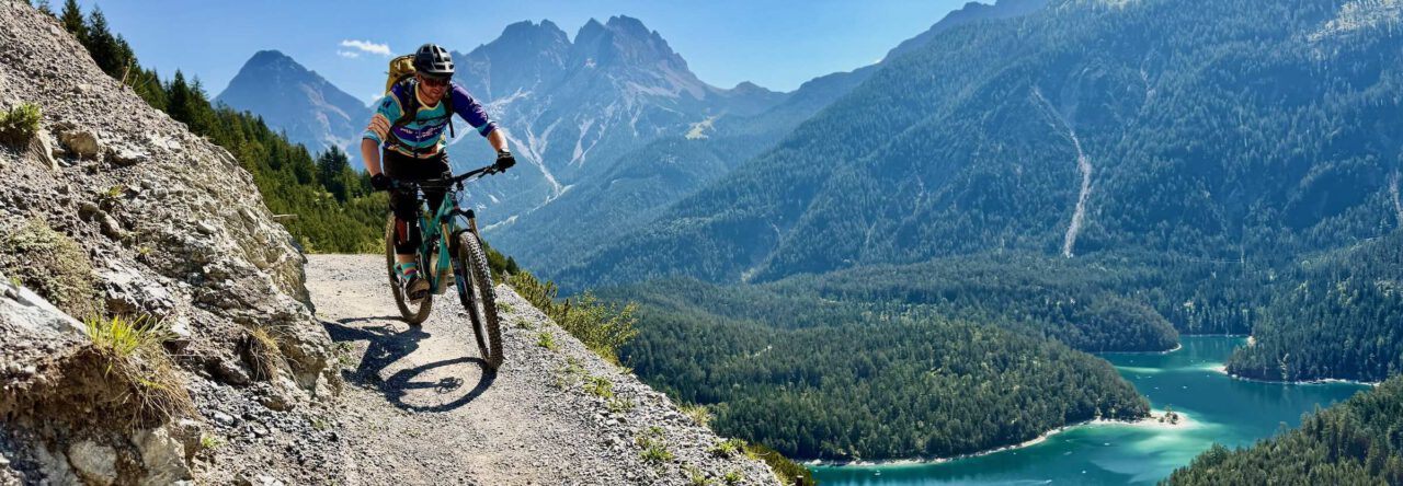 Mountainbiker auf einem alpinen Trail mit Blick auf Bergsee und Alpen Mountainbike Blog mtb-moments.de