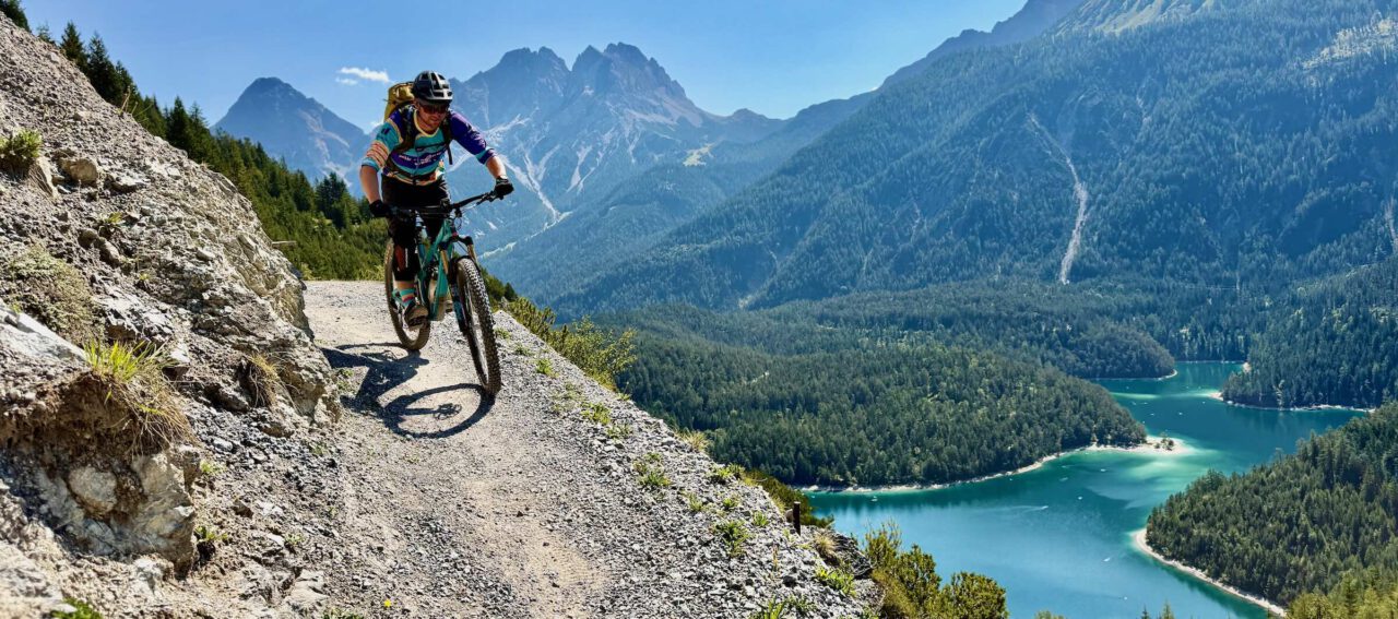 Mountainbiker auf einem alpinen Trail mit Blick auf Bergsee und Alpen